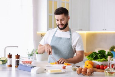 Mutfakta yemek pişirirken tabletten yemek tarifine bakan gülümseyen adam.