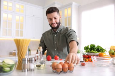 Mutfaktaki masada yemek pişiren gülümseyen adam.