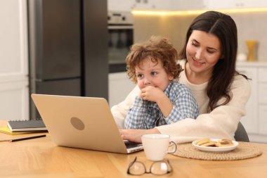 Bilgisayarla çalışan gülümseyen kadın ve oğlu ofis odasındaki tahta masada.