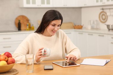 Ofisteki ahşap masada tabletle çalışan gülümseyen kadın.