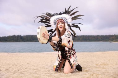 Duygusal şaman kadın Amerikan yerlisi başlıklı yüz boyama ve tef ritüeli yapan açık nehir kıyısında diz çökerek