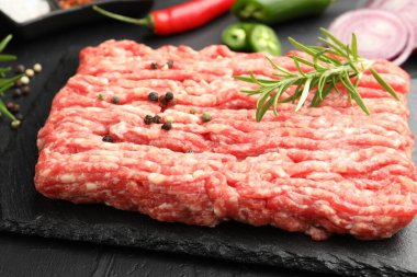 Biberiyeli çiğ et ve siyah masada baharatlar, yakın plan.