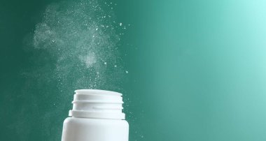 Pouring talcum powder from plastic bottle on green background, closeup. Space for text