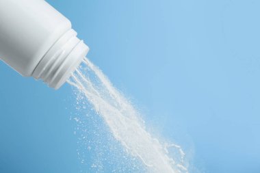 Açık mavi arka planda plastik şişeden talk pudrası dökülüyor, yakın plan. Metin için boşluk