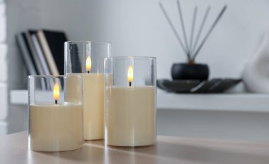 Decorative LED candles on wooden table at home, closeup. Space for text