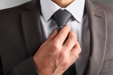 Takım elbiseli adam kravatını gri arka planda düzeltiyor.