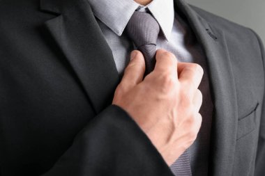 Takım elbiseli adam kravatını gri arka planda düzeltiyor.