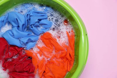 Plastic basin with clothes, water and foam on pink background, top view