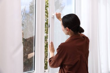 Genç bir kadın evinde modern bir pencere açıyor.