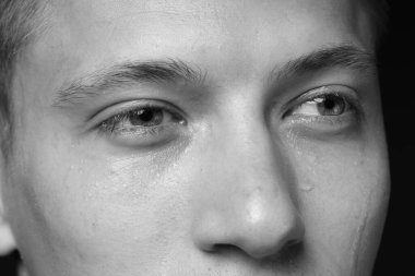 Üzgün adam karanlık arka planda ağlıyor, yakın planda. Siyah ve beyaz etkisi