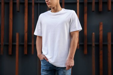 Duvarın yanında beyaz tişört giyen genç adam, yakın plan. Tasarım için model