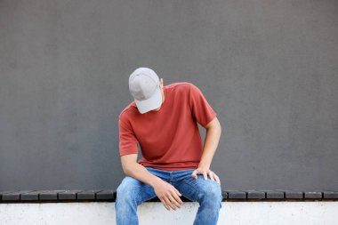 Gri duvarın yanında kırmızı tişört giyen genç adam. Tasarım için model