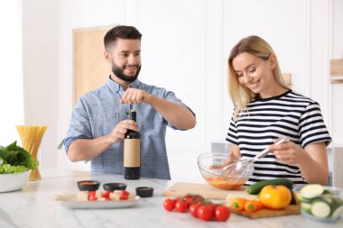 Gülümseyen adam mutfakta karısıyla yemek pişirirken şarap şişesini açıyor.