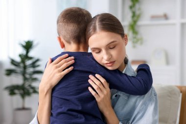 Anne, üzgün oğlunu evde destekleyip kucaklıyor.