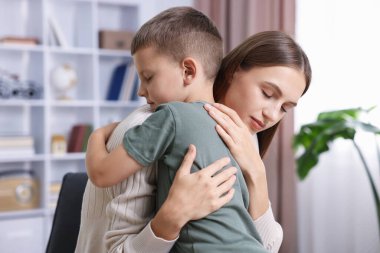 Anne, üzgün oğlunu evde destekleyip kucaklıyor.