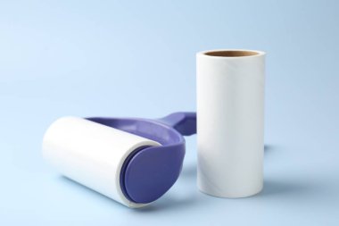 Lint roller and adhesive roll on light blue background, closeup