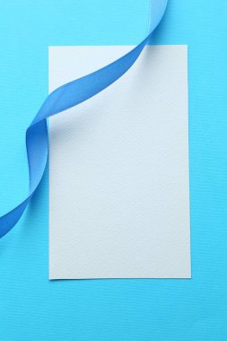 Beautiful ribbon and blank card on light blue background, flat lay