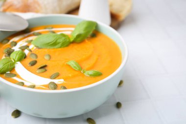 Delicious pumpkin soup served on white tiled table, closeup. Space for text