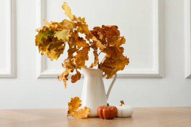 Vase with golden leaves and decorative pumpkins on wooden table. Autumn season
