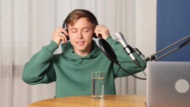 Kulaklıklarda podcast sunucusu. İçerideki ahşap masada talk show 'u kaydediyor. Kamera görüntüsü.