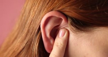 Ses geliyor. Kızıl arka planda kulağına masaj yapan kadın, yakın plan.