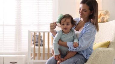 Anne bebeğinin saçını evde koltukta tarıyor.