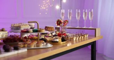 Açık büfe masasının yanında garsonluk. Kapalı mekanda bir sürü tatlı ve içki var. Kamera sola hareket ediyor