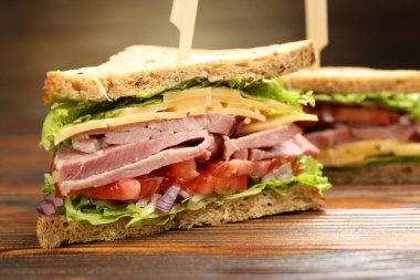Delicious sandwiches with ham, cheese and vegetables on wooden table, closeup