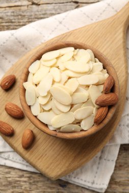Fresh almond flakes and whole nuts in bowl on wooden table, top view