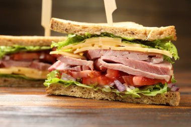 Delicious sandwiches with ham, cheese and vegetables on wooden table, closeup