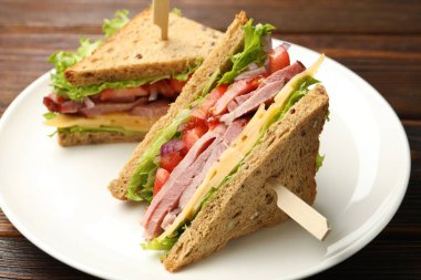 Delicious sandwiches with ham, cheese and vegetables on wooden table, closeup