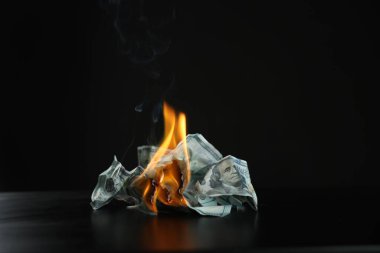 Burning dollar banknotes on black table against dark background