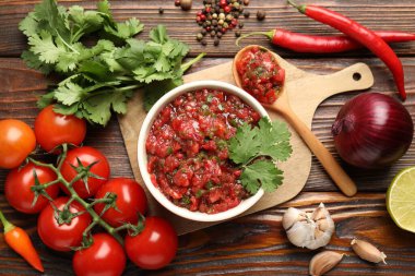 Delicious salsa sauce in bowl and ingredients on wooden table, flat lay