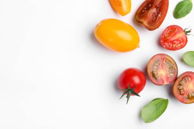 Different ripe tomatoes and basil leaves on white background, flat lay. Space for text
