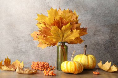 Gri duvarın yanındaki ahşap masada kuru yapraklardan, böğürtlenlerden ve kabaklardan oluşan vazolarla sonbahar kompozisyonu