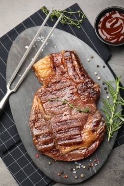 Lezzetli ızgara biftek, otlar, baharatlar, oyma çatal ve ketçap, gri desenli masa, düz uzanma