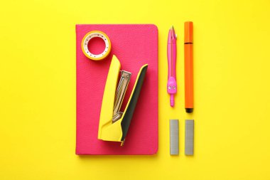 Stapler and other stationery on yellow background, flat lay