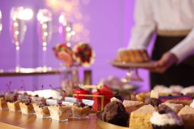 Different delicious desserts on buffet table and waiter, selective focus