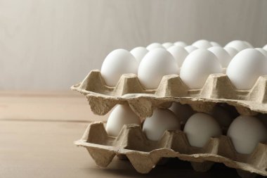 Many raw chicken eggs in cartons on wooden table, closeup