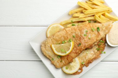 Beyaz ahşap masada soslu, limonlu ve yeşil soğanlı İngiliz Geleneksel Balık ve patates kızartması.