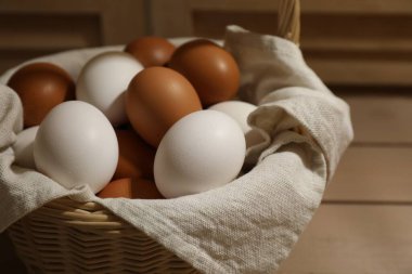 Different raw chicken eggs in wicker basket on table, closeup