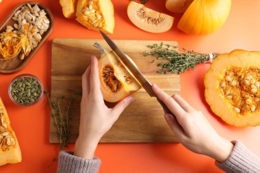 Turuncu arka planda balkabağı kesen kadın.