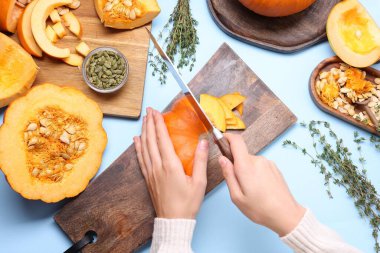 Açık mavi arka planda balkabağı kesen kadın.