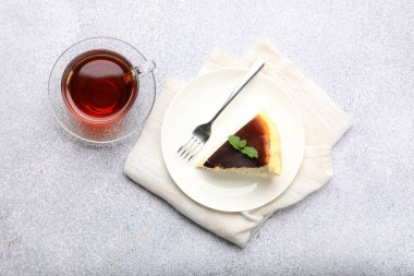 Bir parça leziz Bask peynirli keki, nane şekerli ve açık gri masada çay, düz yatıyordu.