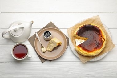 Delicious Basque cheesecake, chocolate sauce and tea on white wooden table, flat lay