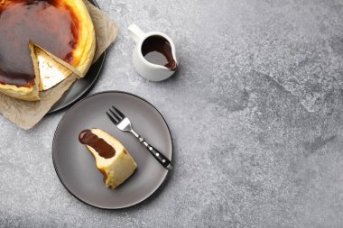 Delicious Basque cheesecake with chocolate sauce and fork on grey table, flat lay. Space for text