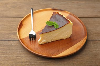 Piece of delicious Basque cheesecake with mint and fork on wooden table, closeup