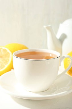 Aromatik çay fincanda, limonlar ve çaydanlık beyaz masada, yakın plan.