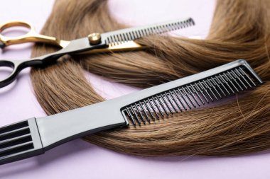 Güzel kahverengi saçlar, makas ve açık mor arkaplan tarağı, yakın plan