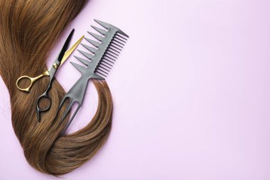 Güzel kahverengi saçlar, makas ve açık mor arkaplan tarağı, üst manzara. Metin için boşluk